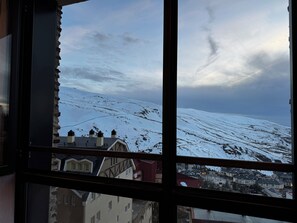 A snowy mountain landscape through a window with a view of a town below. - Snow&sun home (Sierra Nevada)