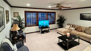 A living room with a sofa, a coffee table, a TV on a stand, a ceiling fan, and a window with blinds. - Cozy 4-bedroom cottage in superb Conneaut with AC (Conneaut)
