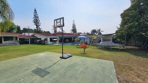 A residential backyard with a basketball hoop, a trampoline, a swimming pool, and a covered patio area. - Villa Cocoyoc for 23 Pax | Pool, Jacuzzi and Basketball Court (Fraccionamiento Lomas de Cocoyoc)