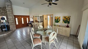 A dining area with a round glass table, wicker chairs, a cabinet with decorative items, and a ceiling fan. - Villa Cocoyoc for 23 Pax | Pool, Jacuzzi and Basketball Court (Fraccionamiento Lomas de Cocoyoc)