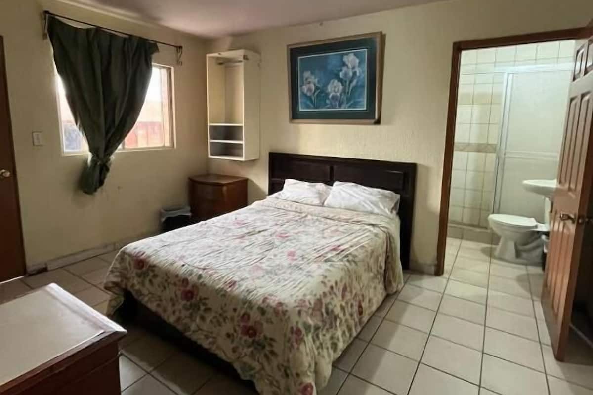 Un dormitorio con cama, escritorio, silla, armario y baño completo con inodoro y ducha.
