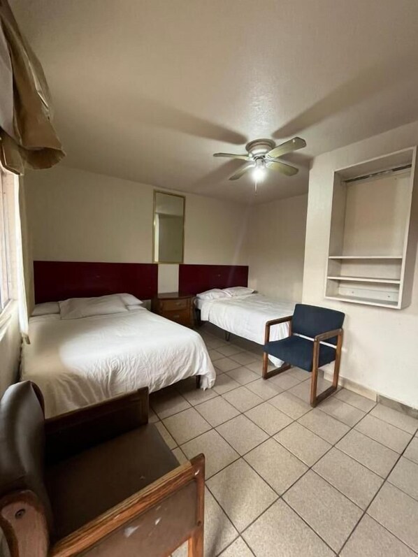 A hotel room with two beds, a chair, a desk, a ceiling fan, and a window. - Hotel Vagabundo (Tijuana)