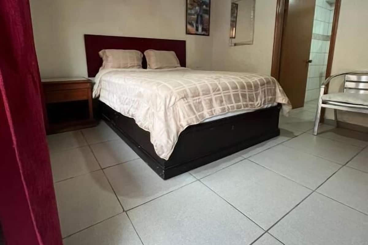 Un dormitorio con cama, mesita de noche, silla, ventilador de techo y puerta.