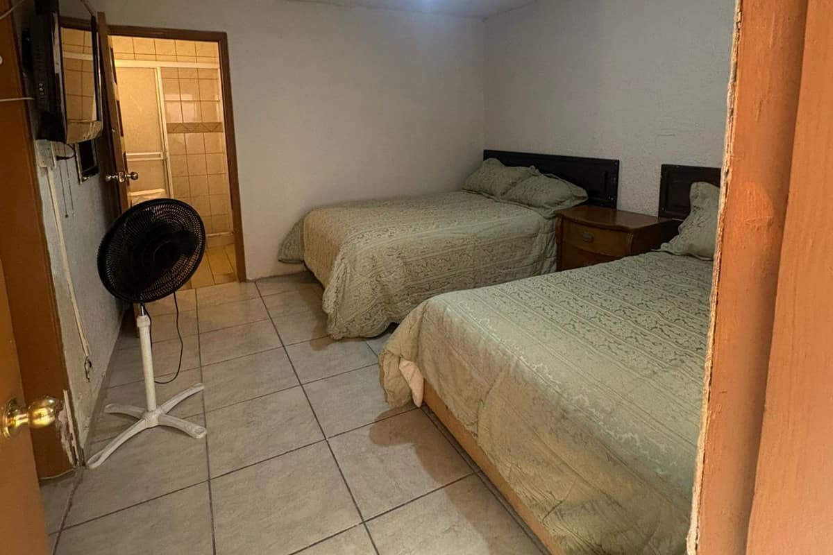 Un dormitorio con dos camas, ventilador de techo, televisor y una puerta que da a otra habitación.