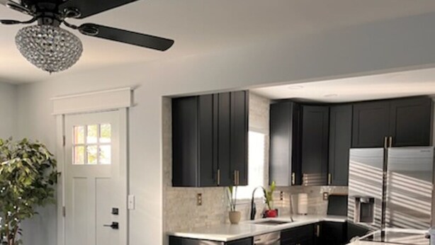 Una cocina moderna con gabinetes oscuros, un refrigerador de acero inoxidable y un ventilador de techo.