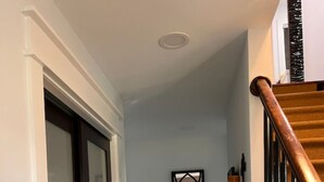 Un pasillo con piso de madera oscura, alfombra estampada, una consola de vidrio con objetos decorativos y una escalera con barandillas de madera.