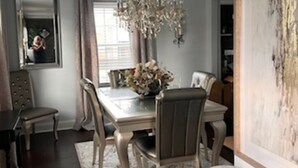 Un comedor con candelabro, una mesa con sillas, una alfombra y un cuadro en la pared.