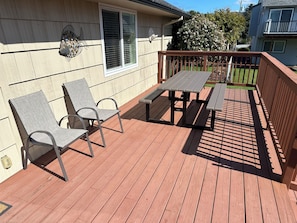 A wooden deck with two chairs and a table, a window with blinds, and a decorative wall piece. - Beautiful 4-BDRM home in Seaside, steps to the beach, perfect family getaway. (Seaside)