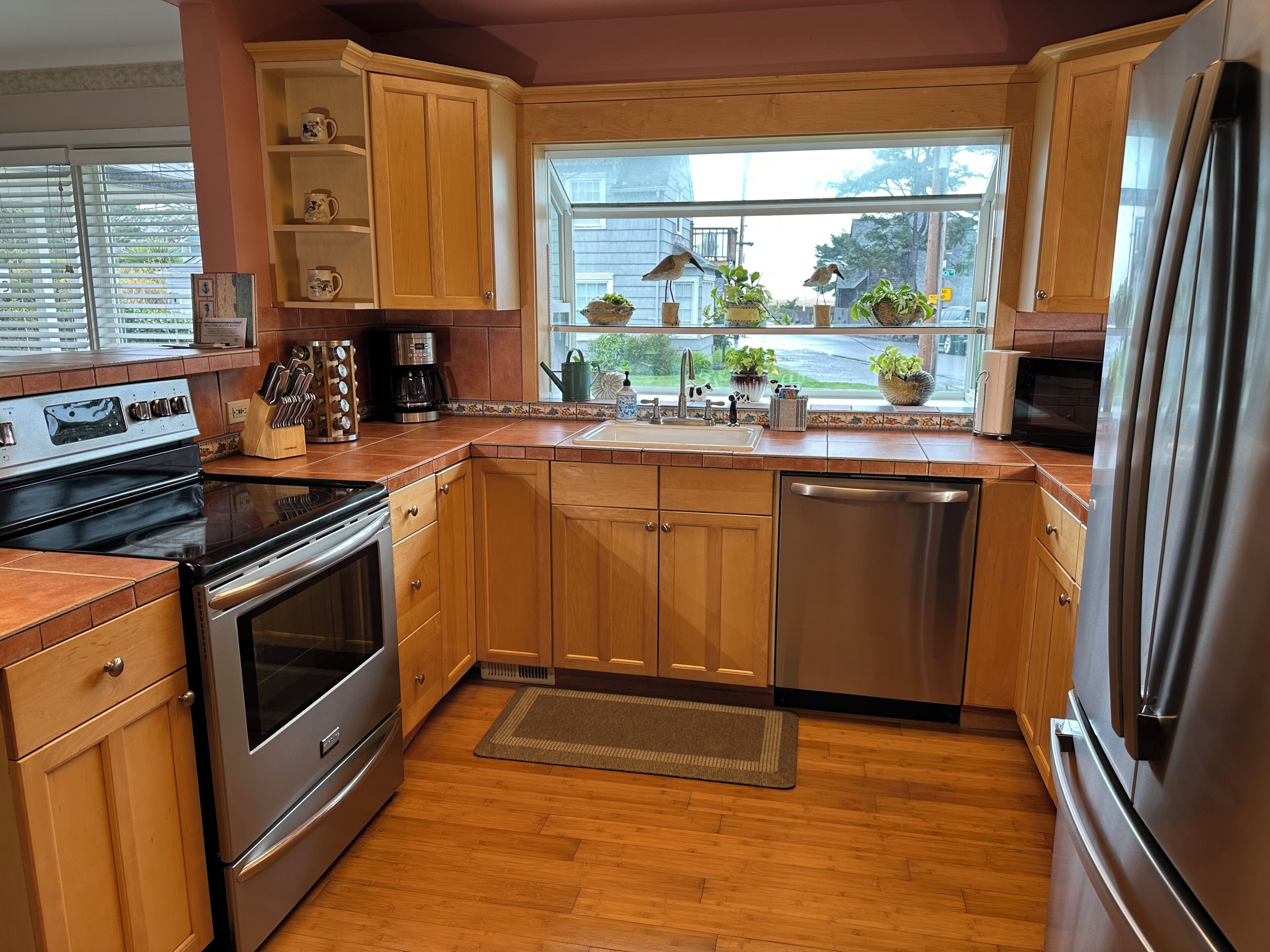 A kitchen with wooden cabinets, a stainless steel refrigerator, a dishwasher, and a window with plants.