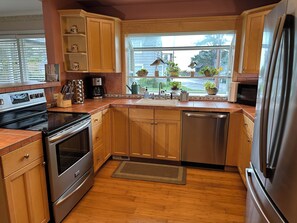 A kitchen with wooden cabinets, a stainless steel refrigerator, a dishwasher, and a window with plants. - Beautiful 4-BDRM home in Seaside, steps to the beach, perfect family getaway. (Seaside)