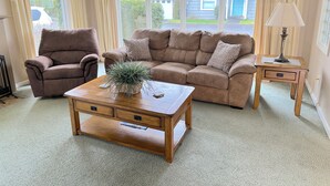 Een woonkamer met een bruine leren bank, een bijpassende fauteuil, een houten salontafel met een plant en een bijzettafeltje met een lamp.