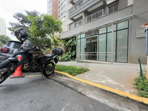 A motorcycle parked in front of a building with a glass facade, a metal railing, and a visible door. - GA 63 Ape com AR prox Allianz e Einstein (São Paulo)