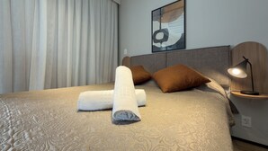 A neatly made bed with rolled towels, a headboard, a bedside table with a lamp, and a wall-mounted abstract artwork. - GA 63 Ape com AR prox Allianz e Einstein (São Paulo)