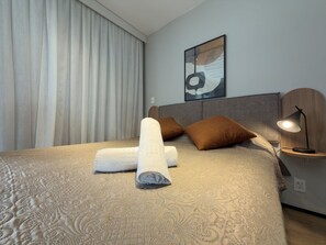 A neatly made bed with rolled towels, a headboard, a bedside table with a lamp, and a wall-mounted abstract artwork. - GA 63 Ape com AR prox Allianz e Einstein (São Paulo)