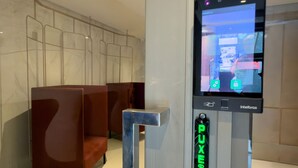 A public restroom with a digital kiosk, a push button, and a seating area. - GA 63 Ape com AR prox Allianz e Einstein (São Paulo)