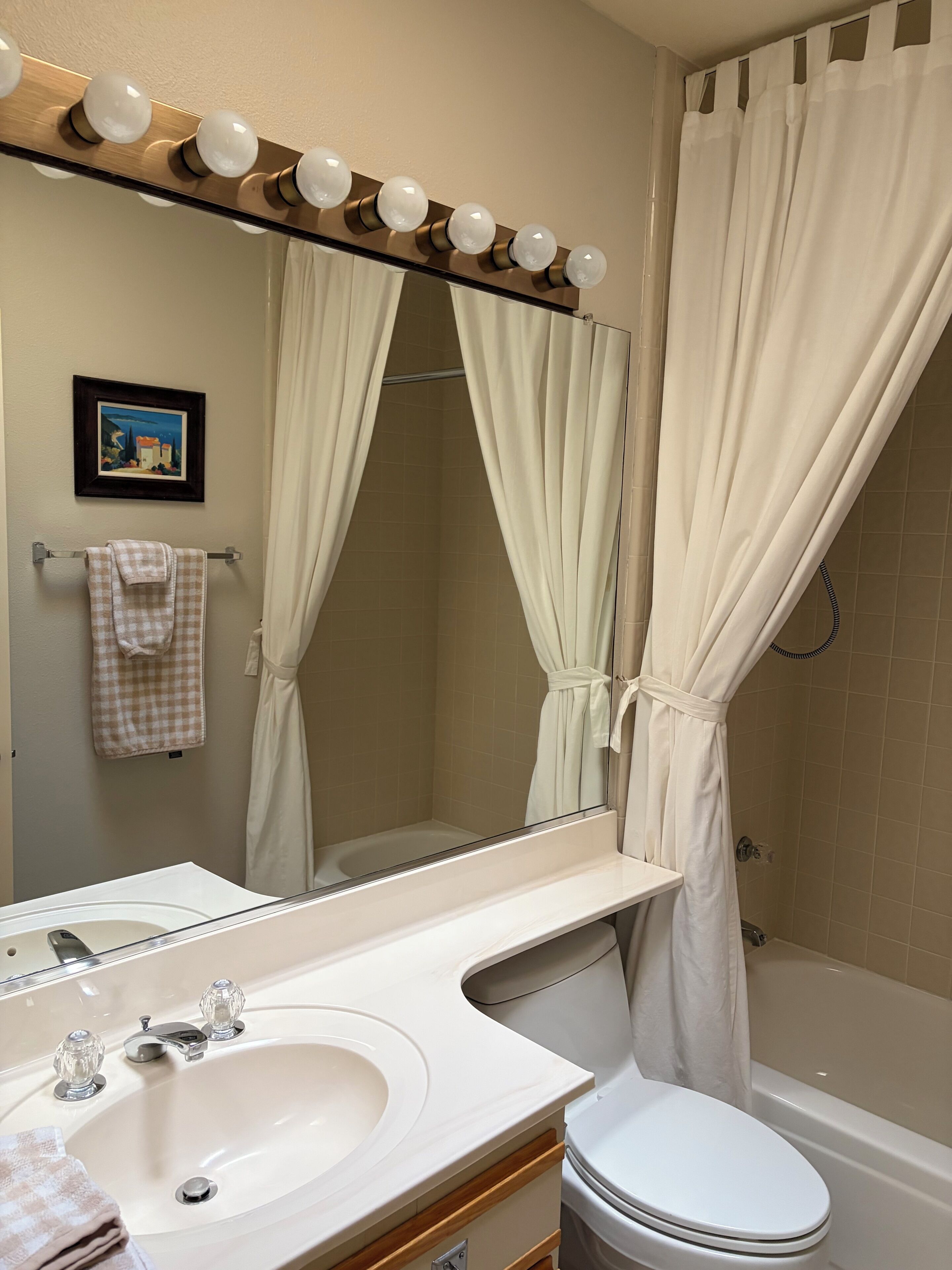Une salle de bain comprenant un lavabo, un miroir, un meuble-lavabo, des toilettes, une baignoire et un rideau de douche.