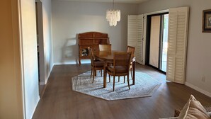 Uma sala de jantar com mesa e cadeiras de madeira, um candelabro e vista através de portas abertas.