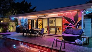 Ein moderner Poolbereich mit einer verglasten Lounge, einem Pool und Gartenmöbeln.
