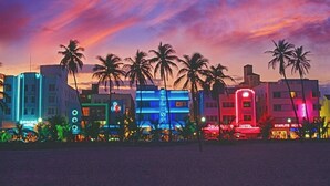 Eine Reihe hell erleuchteter Hotels mit Neonreklame, Palmen und einem Sonnenuntergangshimmel.