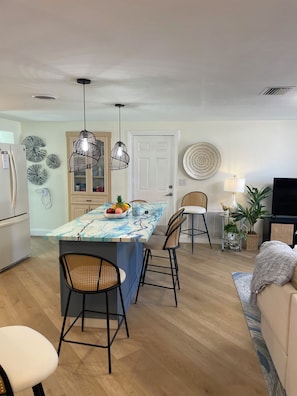 A modern kitchen with a marble island, pendant lights, and a dining area with wicker chairs. - Cozy chic 2-bedroom house in Port Richey with screened in pool (Port Richey)