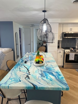 A kitchen with a marble countertop, a fruit bowl, a hanging light fixture, and modern appliances. - Cozy chic 2-bedroom house in Port Richey with screened in pool (Port Richey)