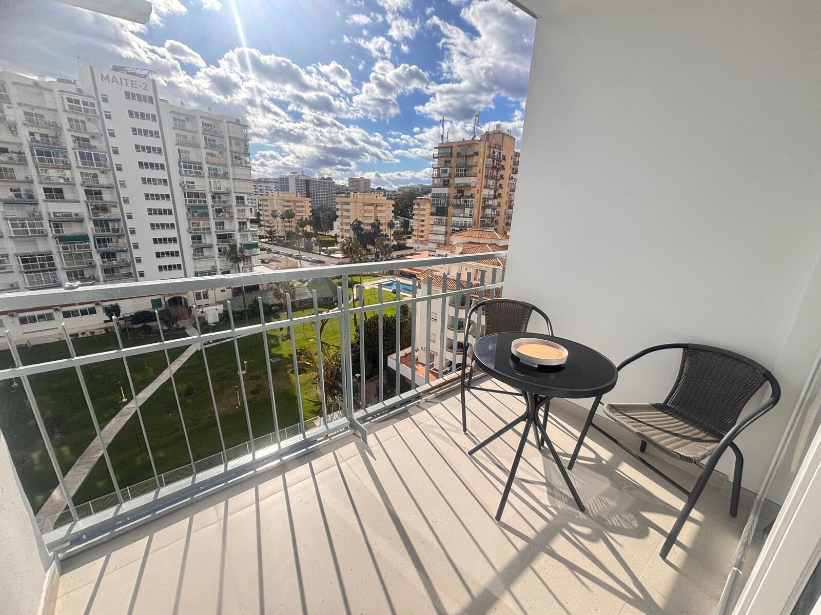 A balcony with a table and chairs, a view of buildings, and a clear sky.