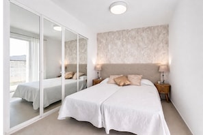 Ein Schlafzimmer mit einem großen Bett, einem Schrank mit Spiegel und Blick durch das Fenster.