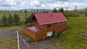 En træhytte med rødt tag, en balkon og et flagstang med et flag.