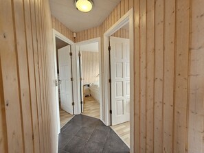 A hallway with wooden paneling, a tiled floor, and white doors leading to a bedroom. - Secret lagoon villa (fludir)