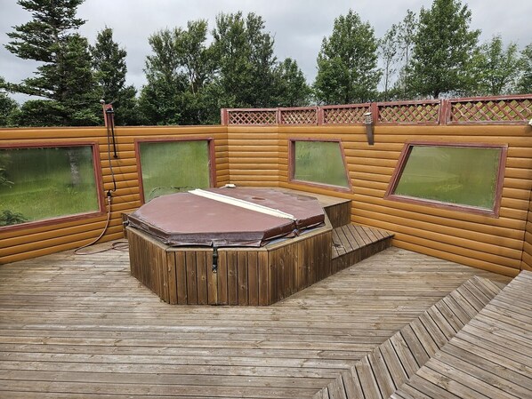 A hot tub in a wooden cabin with large windows and a wooden deck.