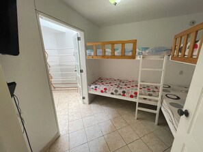 Una habitación con literas, un tendedero y una puerta que da a otra habitación.