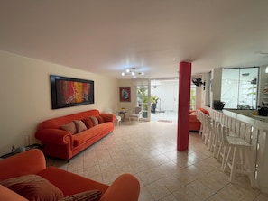 Una sala de estar con un sofá rojo, una zona de comedor con sillas blancas y una cocina con refrigerador.