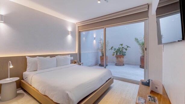 Een moderne slaapkamer met een bed, nachtkastje en uitzicht op een balkon met plantenpotten.