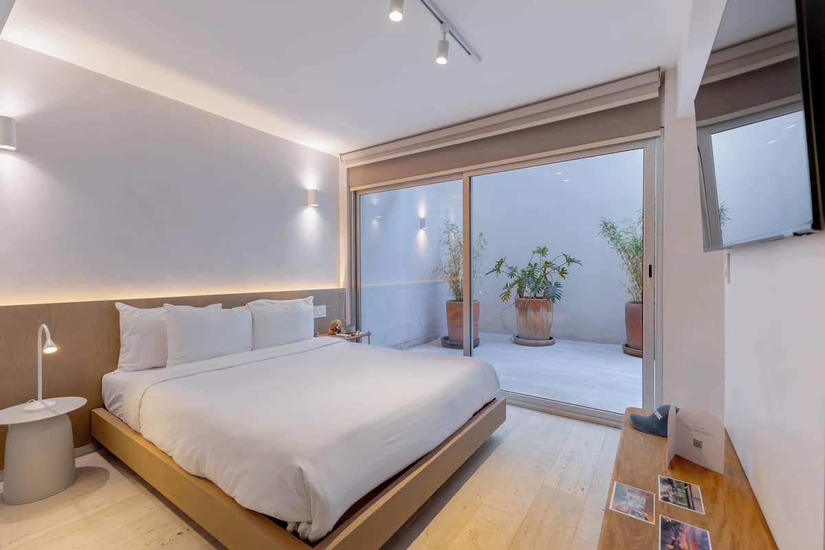 Un dormitorio moderno con cama, mesita de noche y vistas a un balcón con plantas en macetas.