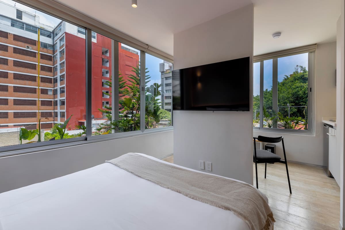 Un hotel moderno con una cama grande, un televisor montado en la pared y vistas de la ciudad a través de amplias ventanas.