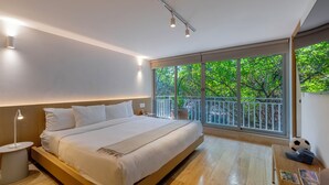Een moderne slaapkamer met een groot bed, nachtkastjes, een raam met uitzicht op groen en een balkon.