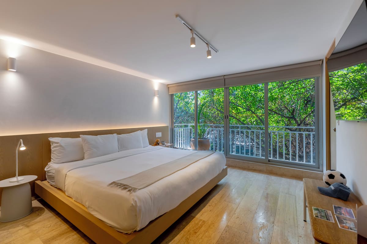Un dormitorio moderno con una cama grande, mesitas de noche, una mesilla auxiliar, una ventana con vistas a zonas verdes y un balcón.