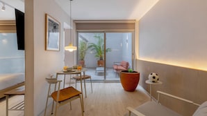 Een moderne kamer met een bed, een bureau, een stoel, een tafel met een plant, en een glazen schuifdeur die leidt naar een buitenruimte met een stoel en een plant.