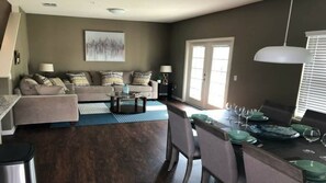 Ein Wohnzimmer mit Sofa, Couchtisch, Esstisch mit Stühlen und einer Küchenzeile mit Fenster.