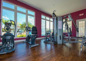 Ein Fitnessstudio mit Cardiogeräten, Gewichten und großen Fenstern mit Blick auf Palmen.