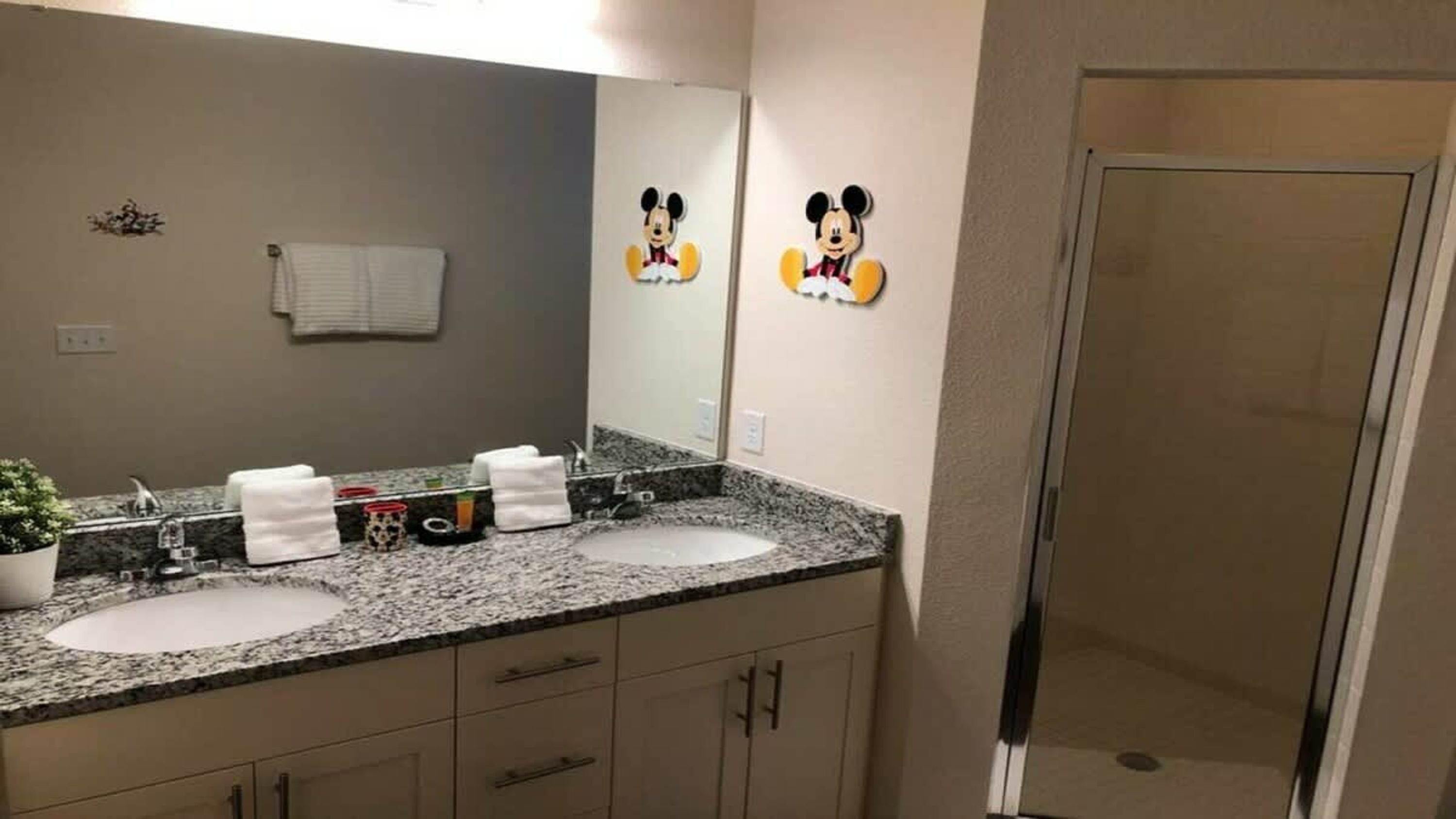 Une salle de bain avec deux lavabos, un miroir et des décorations à l’effigie de Mickey Mouse.