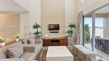 Una sala de estar moderna con un juego de sofá, una mesa de centro, un televisor montado en la pared y dos plantas en macetas.