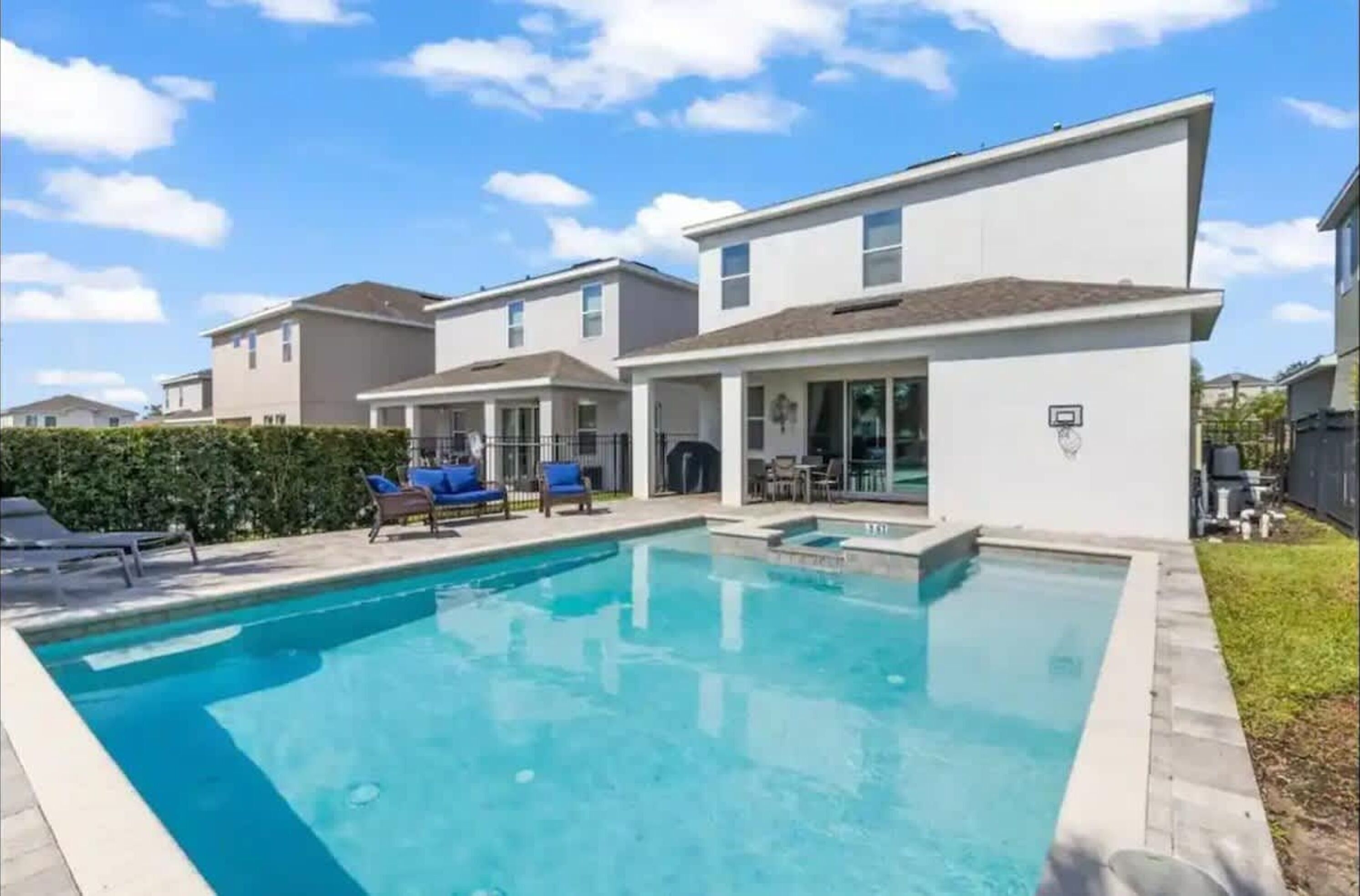 A residential pool area with a swimming pool, lounge chairs, and a covered patio.