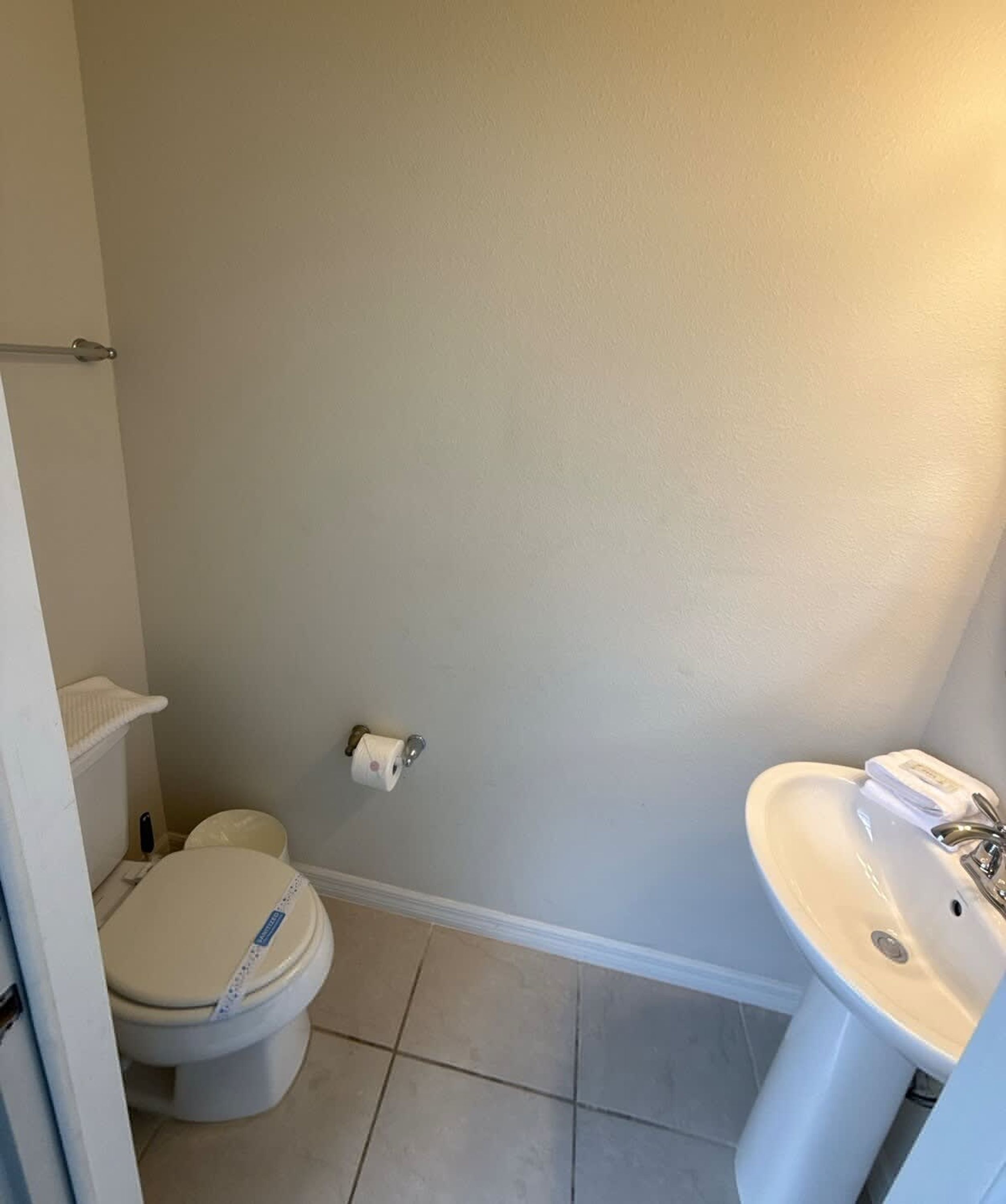 Un baño con inodoro, lavamanos y un dispensador de papel higiénico en la pared.