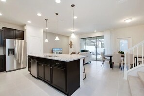 A modern kitchen with dark cabinetry, a large island, and pendant lighting. - Cozy and Spacious 5BR With Pool Near Disney Parks (Kissimmee)