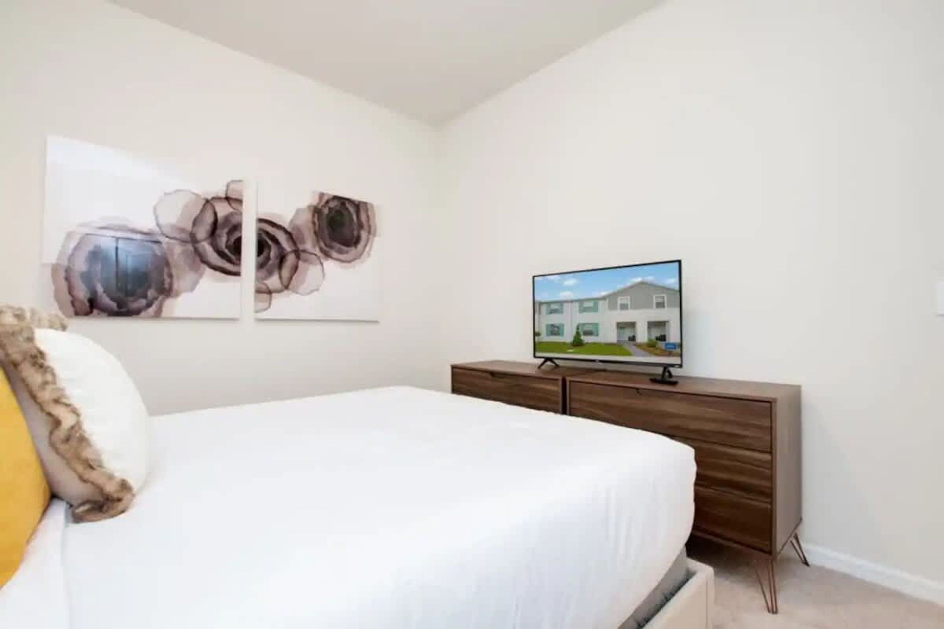 Une chambre à coucher comprenant un lit, une commode, un téléviseur et des œuvres d’art abstraites accrochées au mur.
