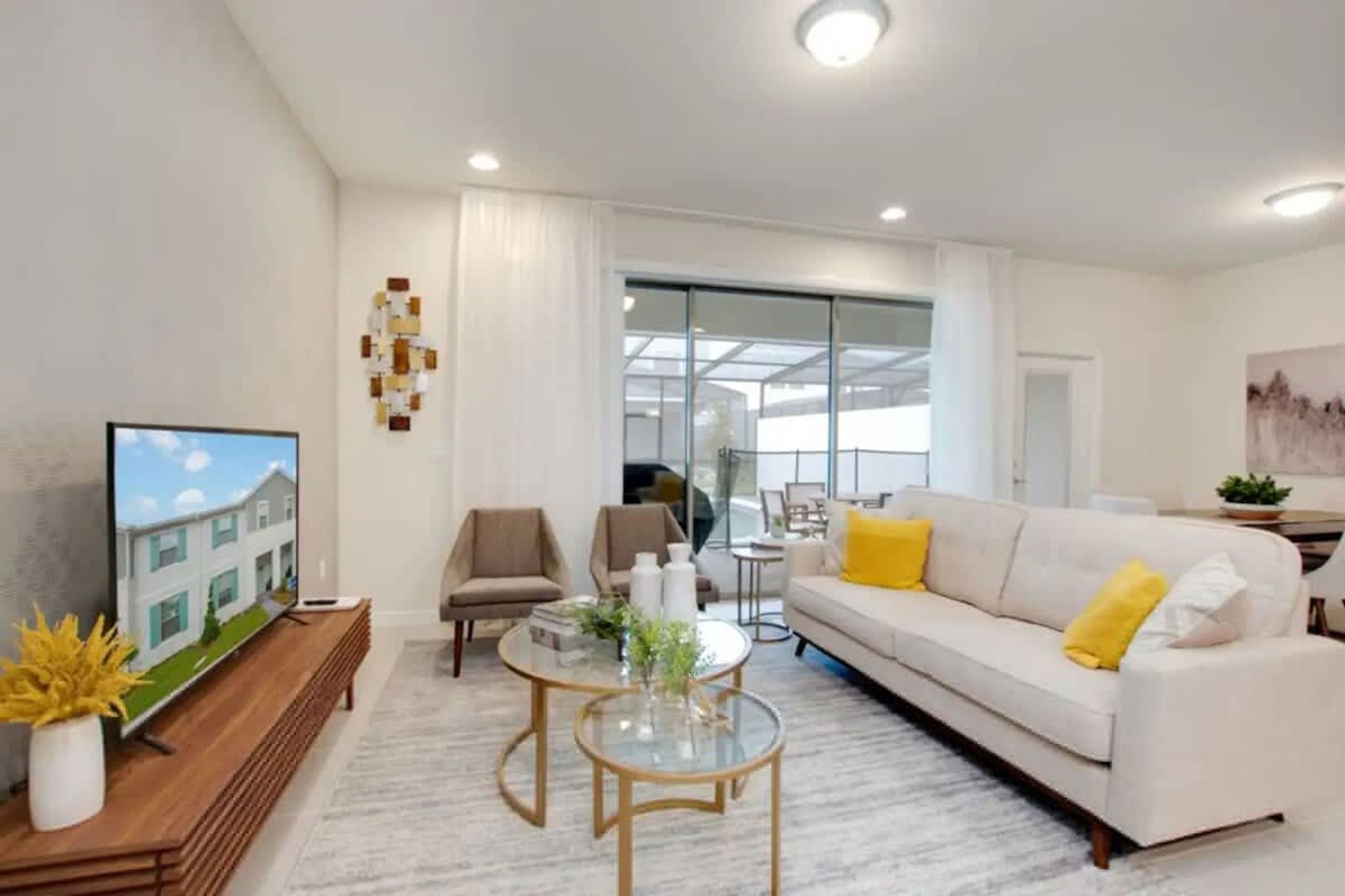 A modern living room with a flat-screen TV, a sofa with yellow cushions, a coffee table, and a glass door leading to a balcony.