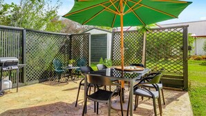 A patio with a table, chairs, a grill, and a green umbrella.