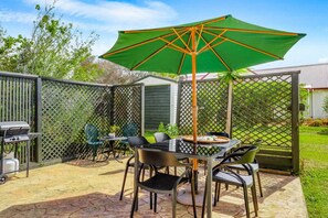 Eine Terrasse mit Tisch, Stühlen, einem Grill und einem grünen Sonnenschirm.