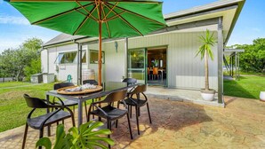 A patio with a table and chairs, a green umbrella, and a house in the background.